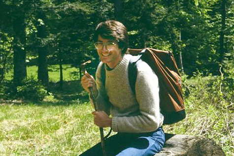 Young Michael Biggins with a backpack, with forest behind.