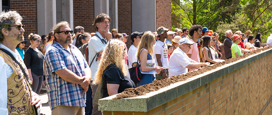 A crowd stands facing the sun outside Meany Hall. 
