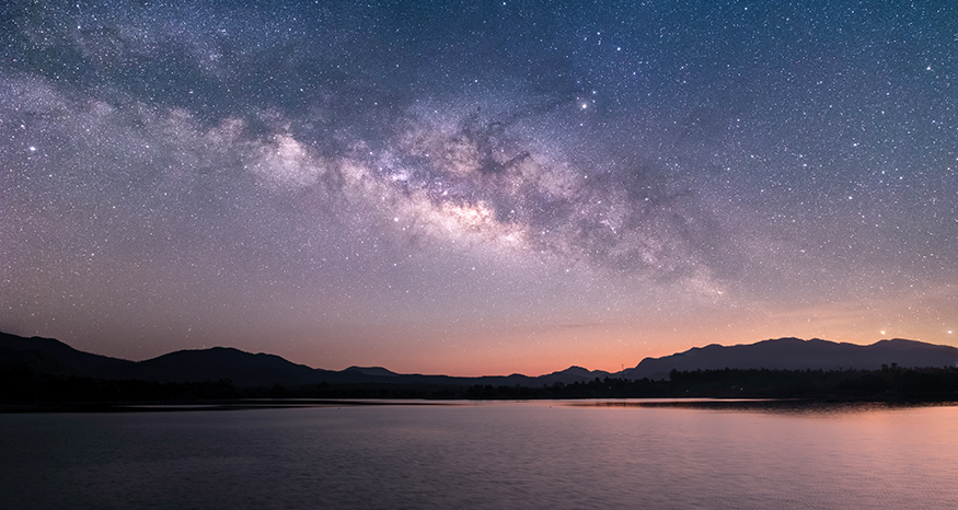 Sunset on a starry night, with calm water in the foreground.