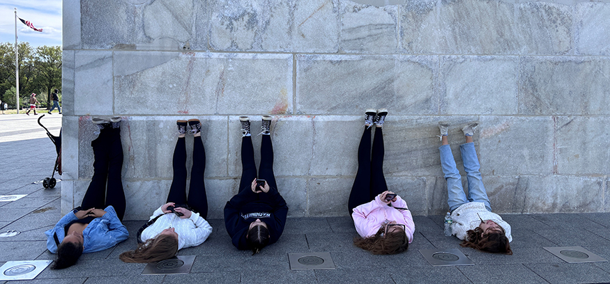 Five students with the backs on the ground and their legs propped against the base of the Washington Monument. 