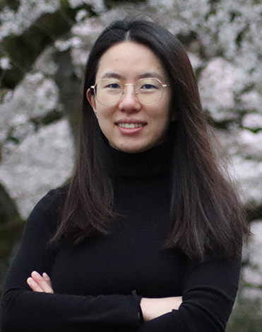 portrait photo of Jieyu Zhou with a blooming cherry tree in the background.
