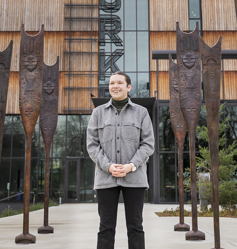 Student standing in front of the Burke Museum between an outdoor art installation