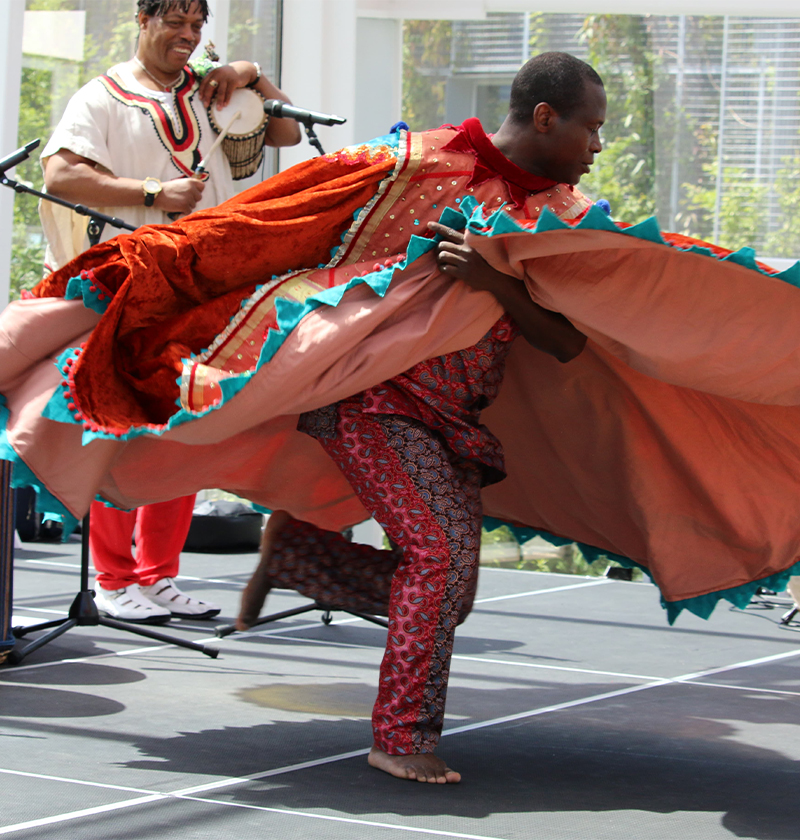 Person dances and spins bright red costume while another person plays a hand drum in the background.