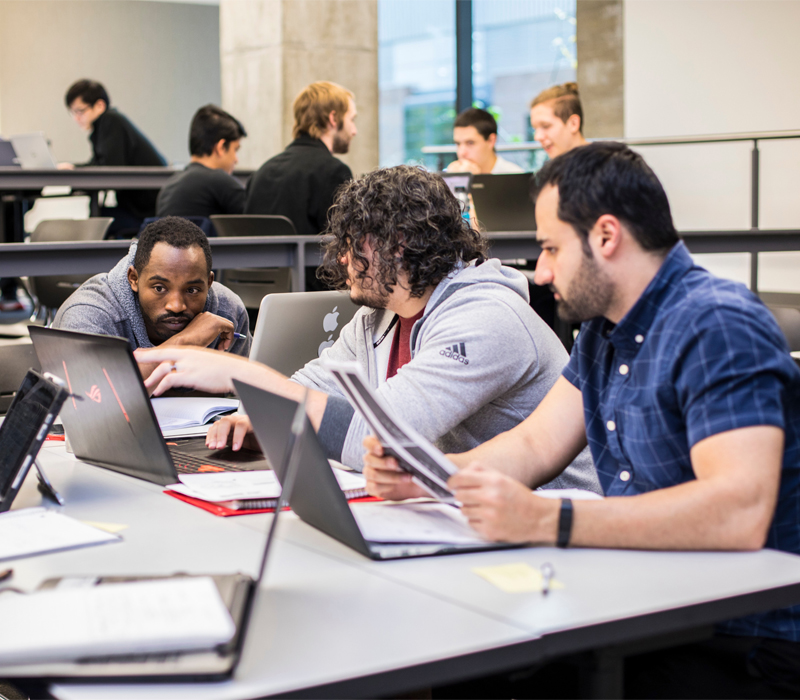 Three students working on their computers in a classroom