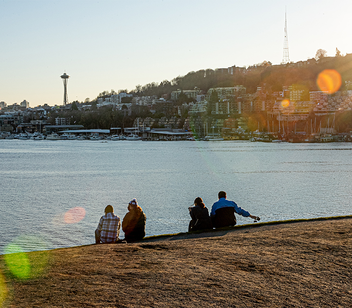 People sitting at the shore of Lake Union, with the Space Needle in the distance.