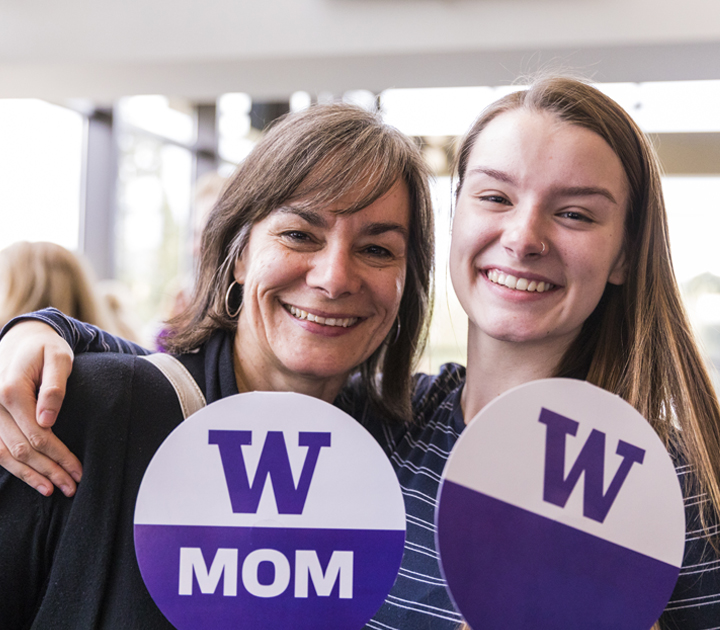 A student and parent holding UW fans smiling at a family event.