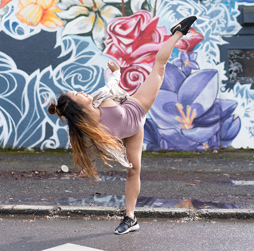 Cheryl Delostrinos doing high leg kick in front of a street mural