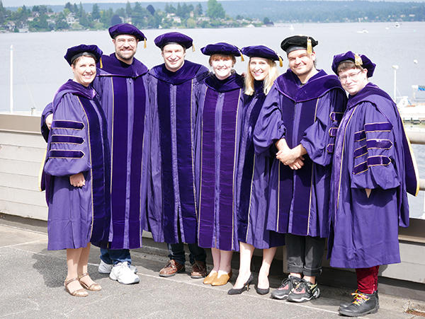 Seven 2019 PhD graduates in purple caps and gowns