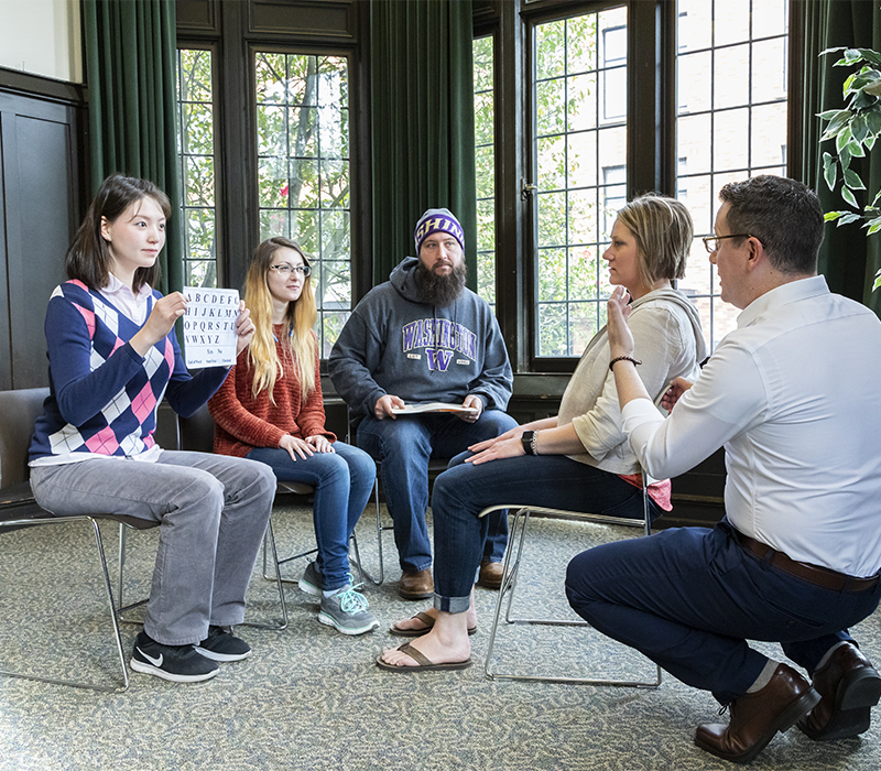 Teacher kneeling and talking with group of students working on speech practices