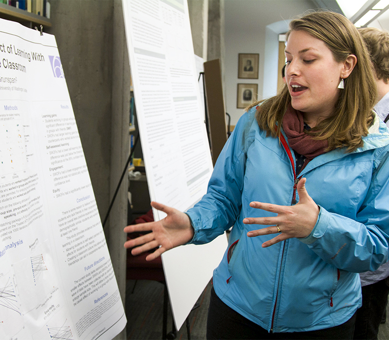 Student in blue jacket talking and gesturing towards poster board