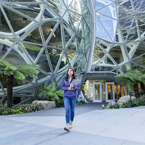 Female student walking with laptop in front of Amazon spheres