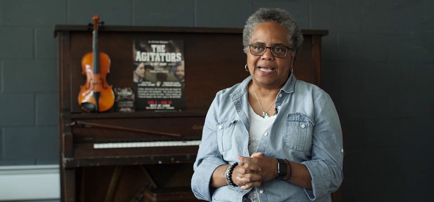 Valerie-Curtis Newton speaking in front of a piano.