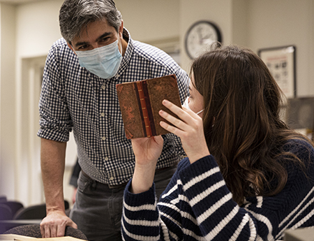 Professor Geoff Turnovsky and a student look at a small book in UW Special Collections. 