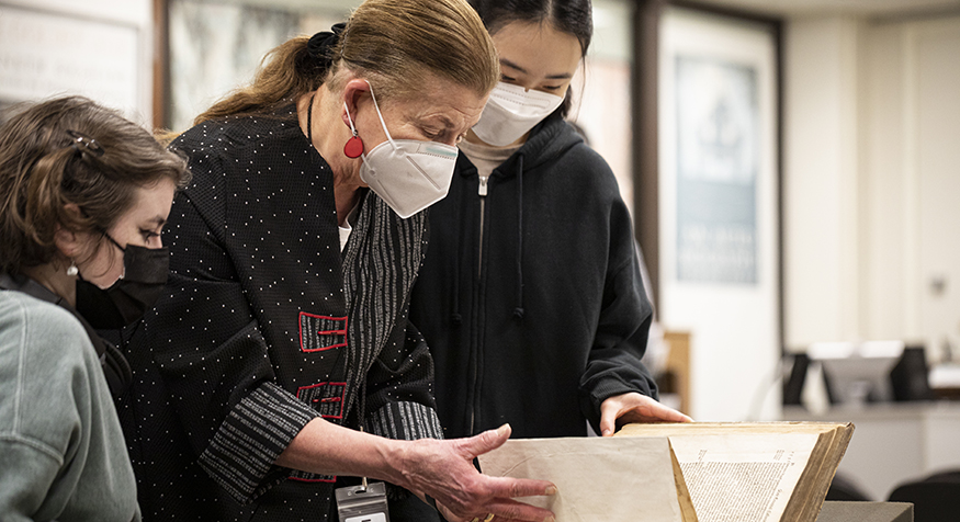 UW Special Collections librarian Sandra Kroupa looking at a old book with two students. 