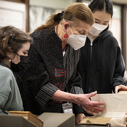 UW Special Collections librarian Sandra Kroupa looking at a old book with two students. 