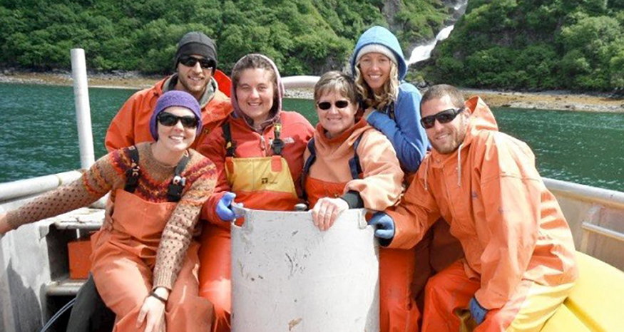 Six adults on fishing boat, all in orange waterproof layers.