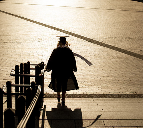 Student in graduation cap & robe walking on campus.