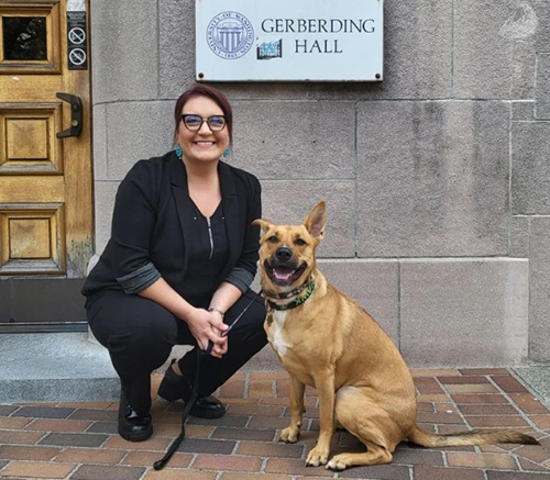 Sherri Bedine outside Gerberding Hall with her dog seated beside her.