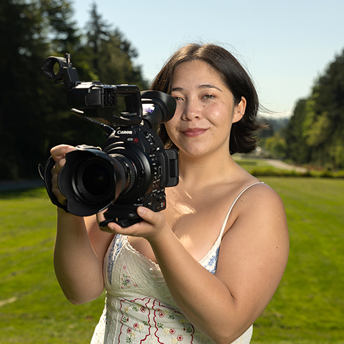 Kenna Fojas on the UW campus, holding a film camera to her face. 
