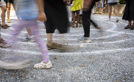Blurred feet walking around a circular labyrinth marked with chalk.