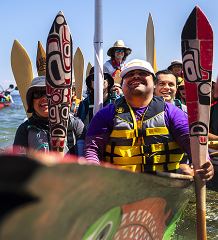 Members of UW's canoe family holding their paddles as the their canoe nears its destination. 