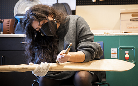 A canoe family member carving a paddle