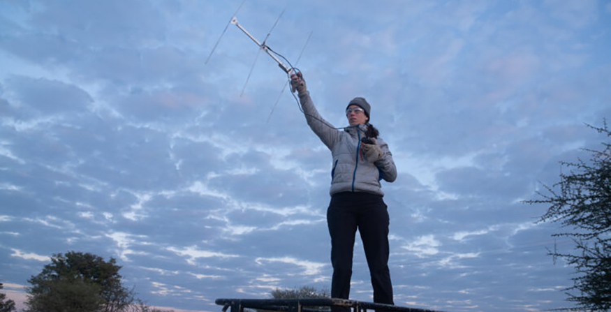 Briana Abrahams standing against a cloudy sky, holding an antenna skyward