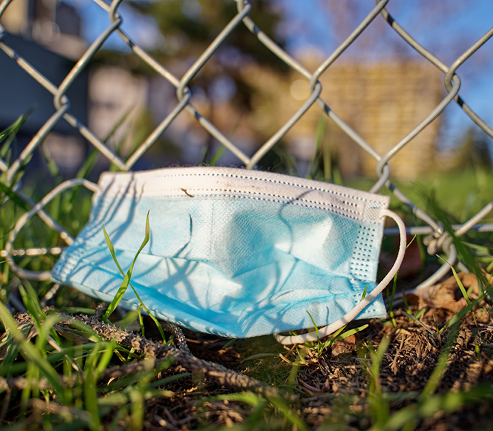 A discarded Covid mask by a chain link fence