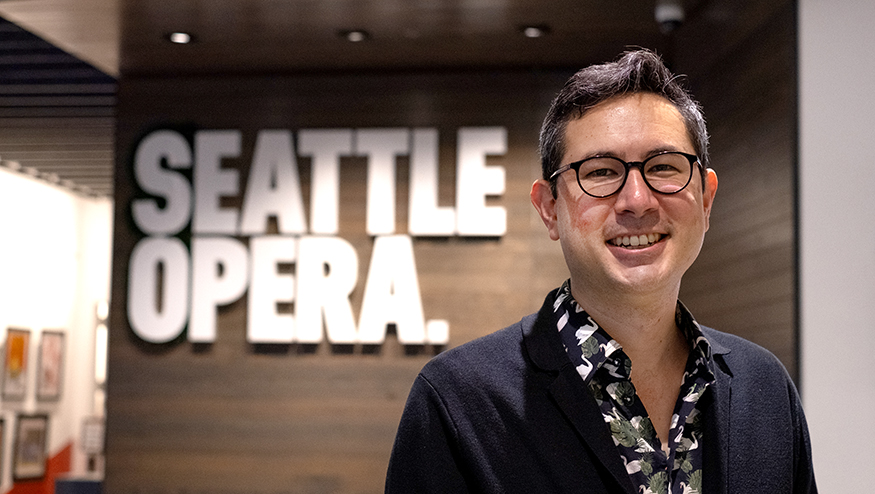 Alex Minami with Seattle Opera sign on the wall behind him