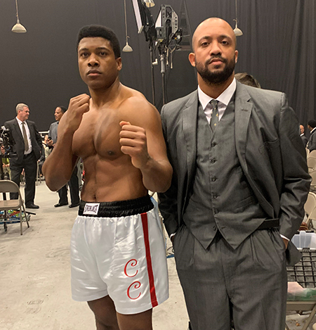 Tre Cotten standing next to actor Eli Goree, who's dressed in boxing shorts as Muhammad Ali.