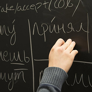 Hand writing words in a foreign language on black chalkboard.