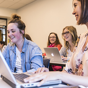 Students in a classroom with laptops open.