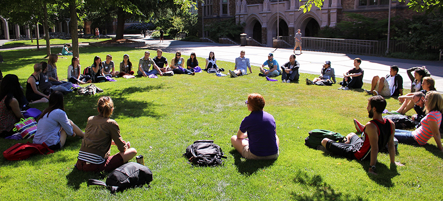 UW class seated in a circle on a lawn outside on sunny day