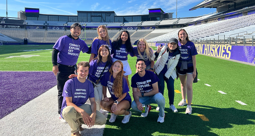 Group of 10 students gathered for photo in Husky Stadium, all wearing UW Orientation t-shirts.