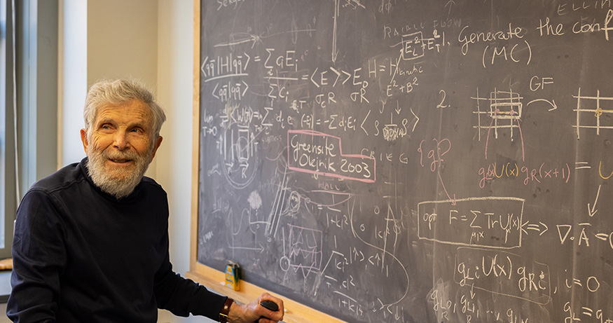 Marshall Baker standing next to a chalkboard with physics notations