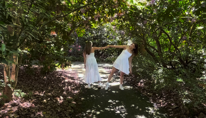 Two women in white, dancing in-between trees on the UW campus. 