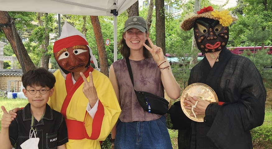 Katie Ruesink and Hojun pose with two performers in masks and traditional clothing at a festival in Korea. 