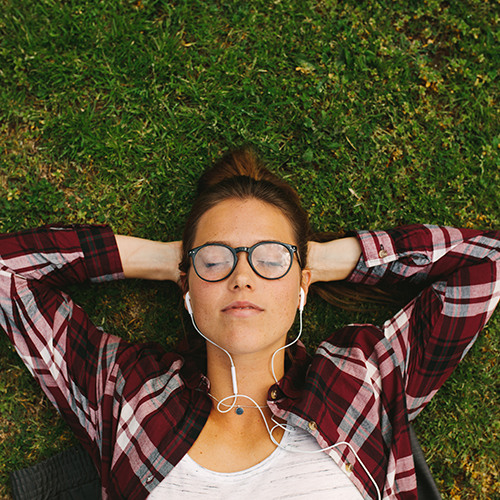 Person laying in the grass, eyes closed, listening to music through headphones