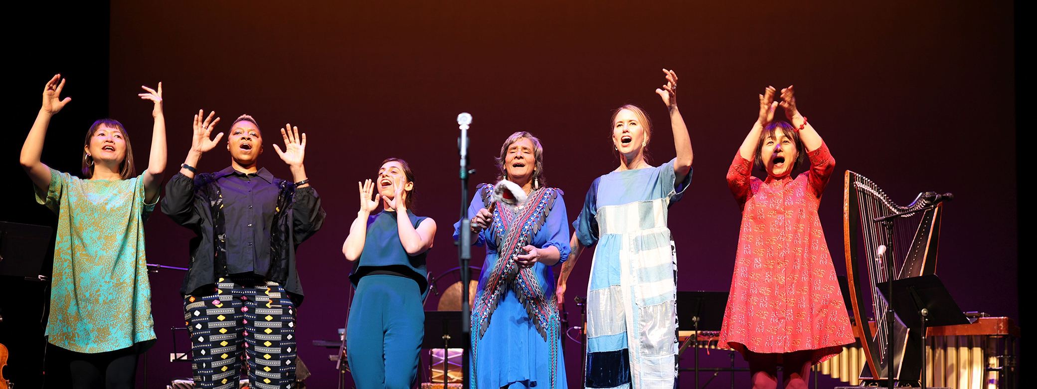 Six members of the Silk Road Ensemble singing onstage, their arms raised. Photo credit: NoirPrism.