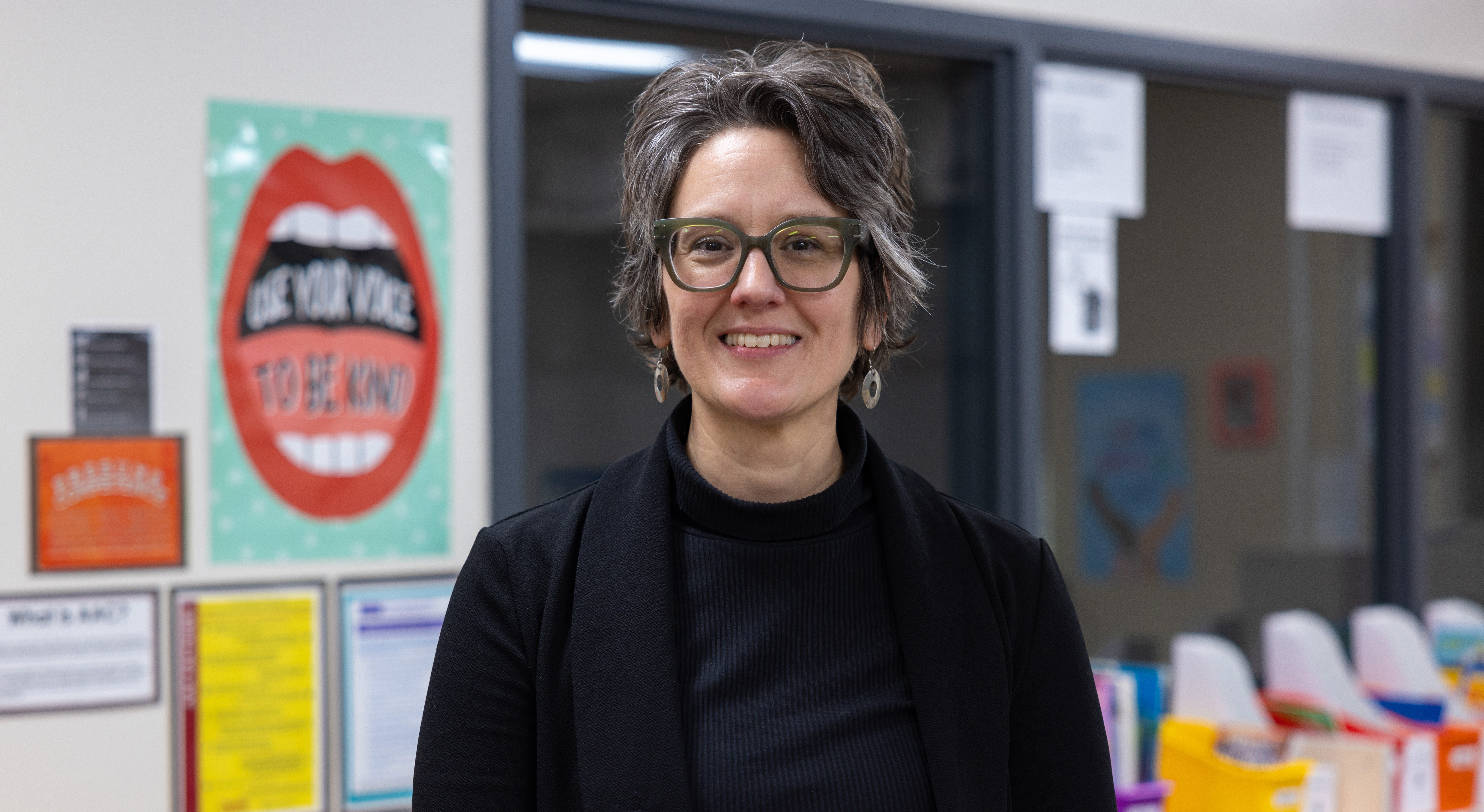 Sara Jerger stands in a classroom with colorful posters on the wall behind her.