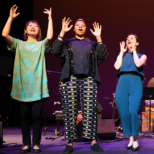 Members of the Silk Road Ensemble singing onstage, their arms raised. Photo credit: NoirPrism.