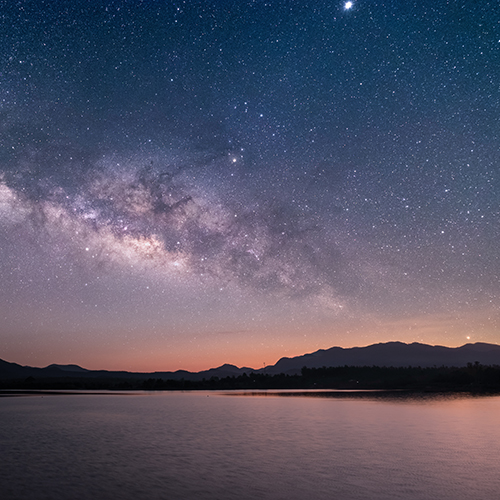 Sunset on a starry night, with calm water in the foreground.