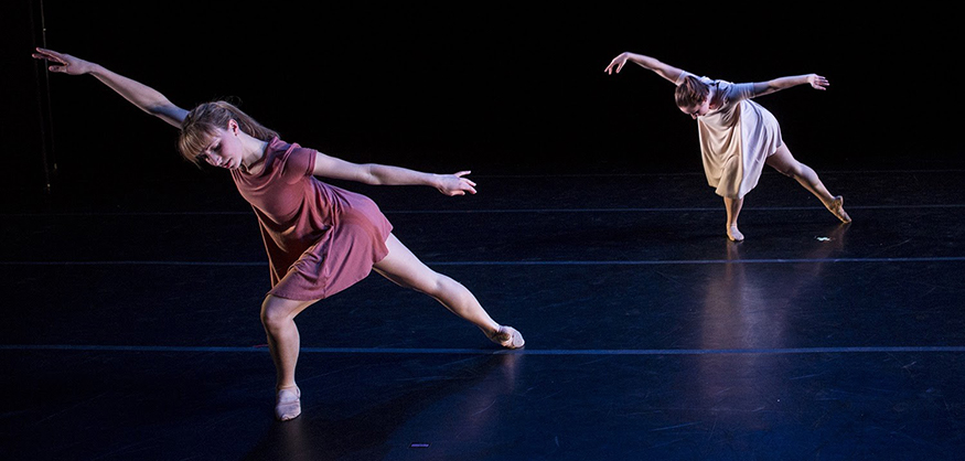 Two dancers performing against a black background, with their arms outstretched