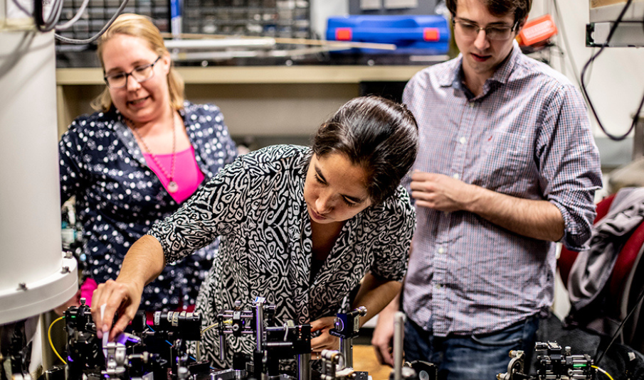 Kai-Mei Fu (center) adjusts equipment for a quantum experiment. Fu's research group studies the quantum-level properties of crystalline materials. Photo by Dennis Wise/University Photography.