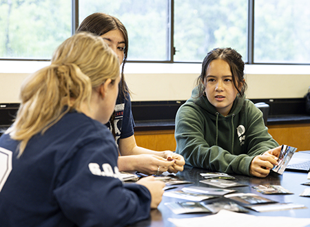 Three students at a round table, looking a photos spread out on the table.