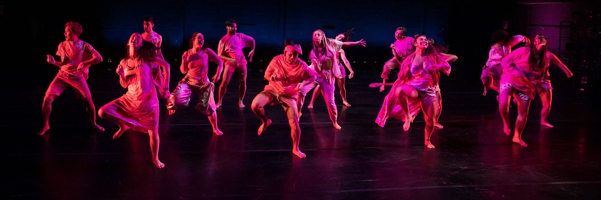 Dancers performing on stage, with light casting a pink/purple glow on them. Photo by Warren Woo.