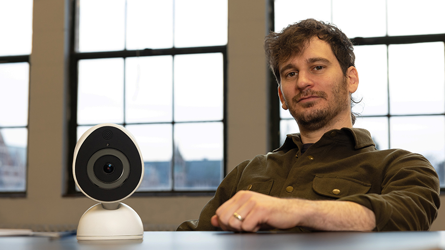 James Pierce in his office with a small, round, portable home surveillance camera on his desk