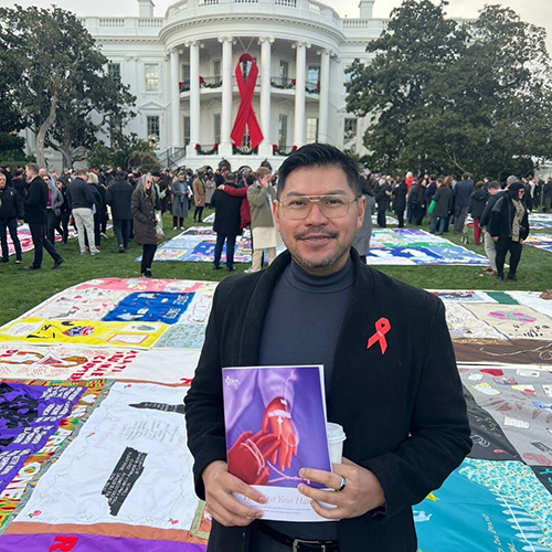 Paulo Pontemayor outside the White House, with the AIDS Memorial Quilt spread out on the lawn behind him. 