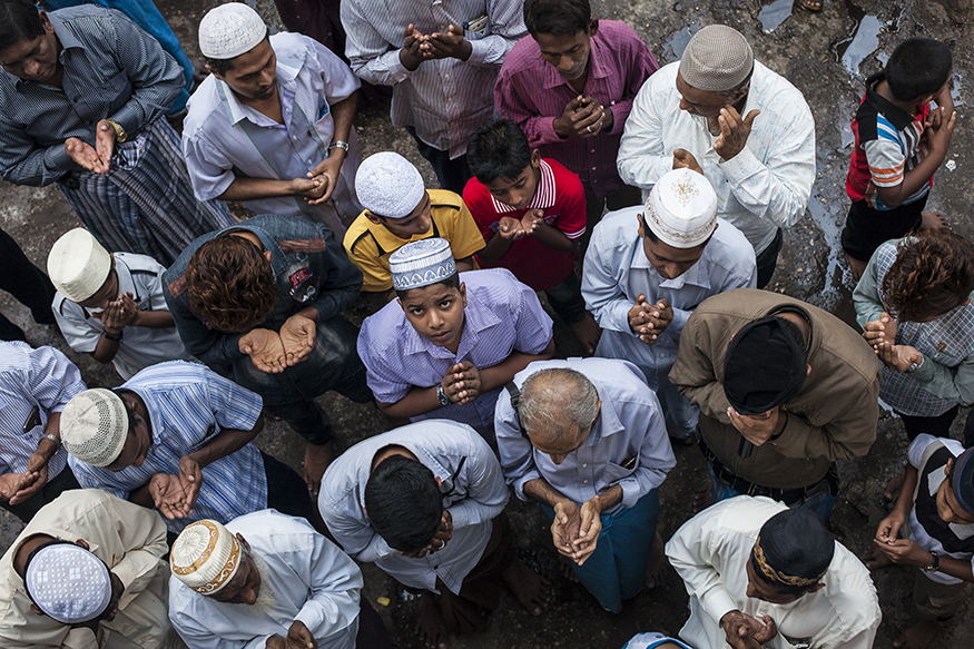 A crowded group of men in prayer, with one looking up at the camera.