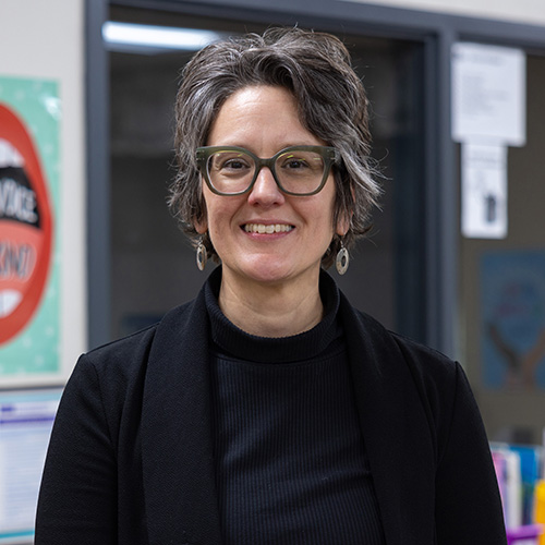 Sara Jerger stands in a classroom with colorful posters on the wall behind her.